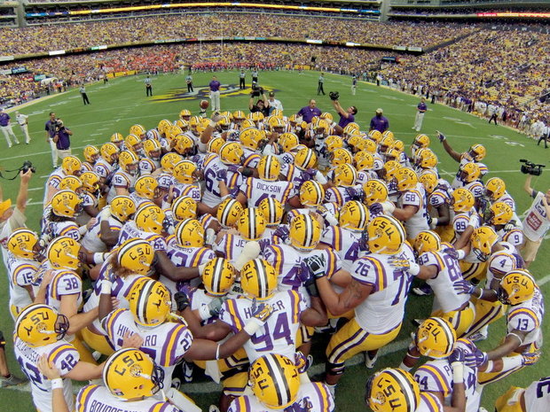 LSU football team members gather on field pregame for group huddle.